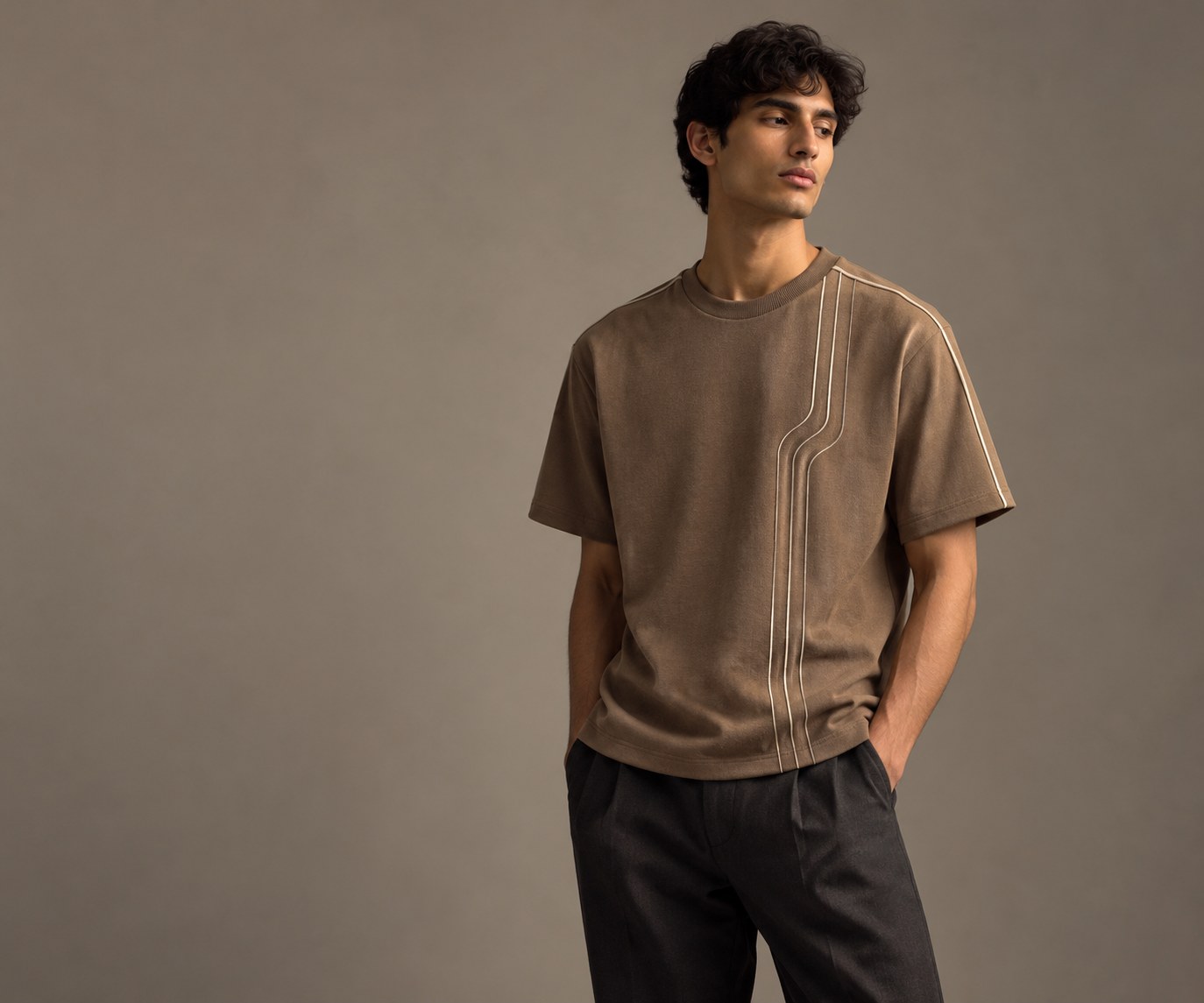 Editorial concept image of a lean-built model wearing a warm taupe T-shirt with subtle cream detailing